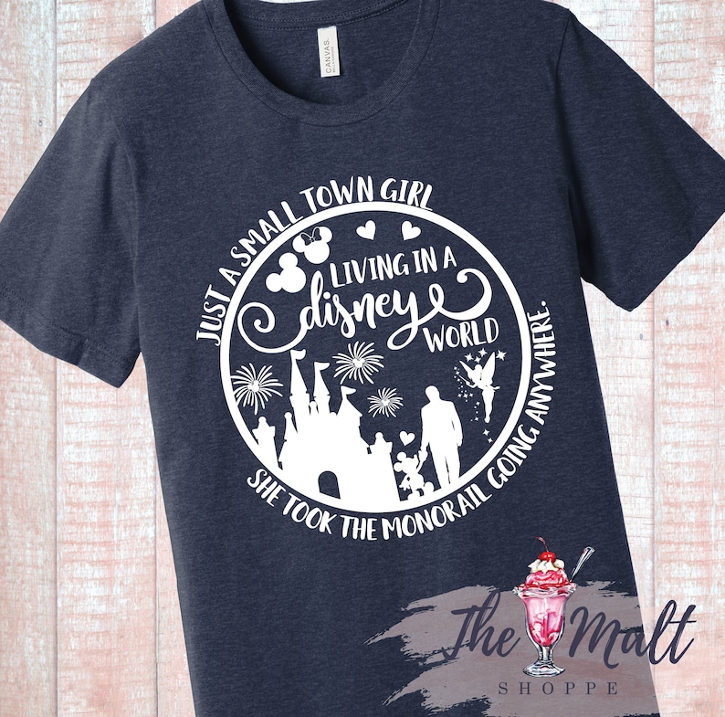 May include: A navy blue t-shirt with a white graphic design. The graphic features a circle with the text "Just a small town girl living in a disney world" and a silhouette of Cinderella's castle, fireworks, Mickey Mouse, Tinkerbell, and a family.