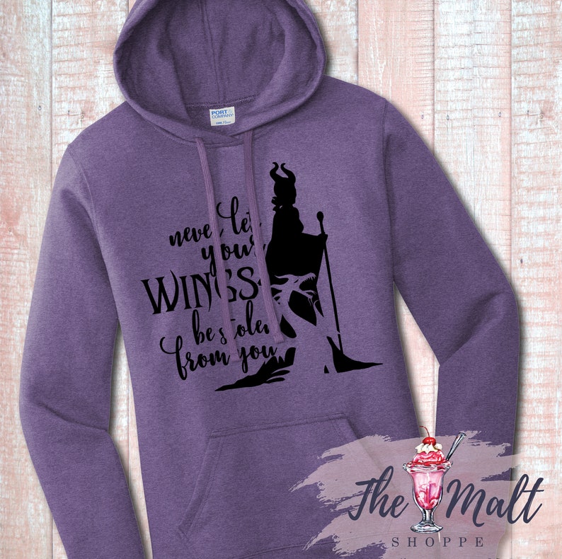 Pu&ograve; includere: Felpa con cappuccio viola con una silhouette nera di Malefica de La Bella Addormentata nel Bosco di Disney. Il testo recita "Non lasciare mai che ti rubino le ali."
