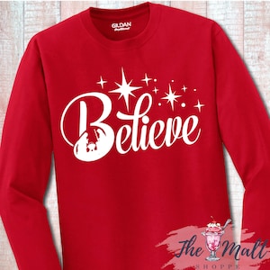 May include: Red long-sleeve shirt with a white design of a star and the word "Believe" with a silhouette of the nativity scene.