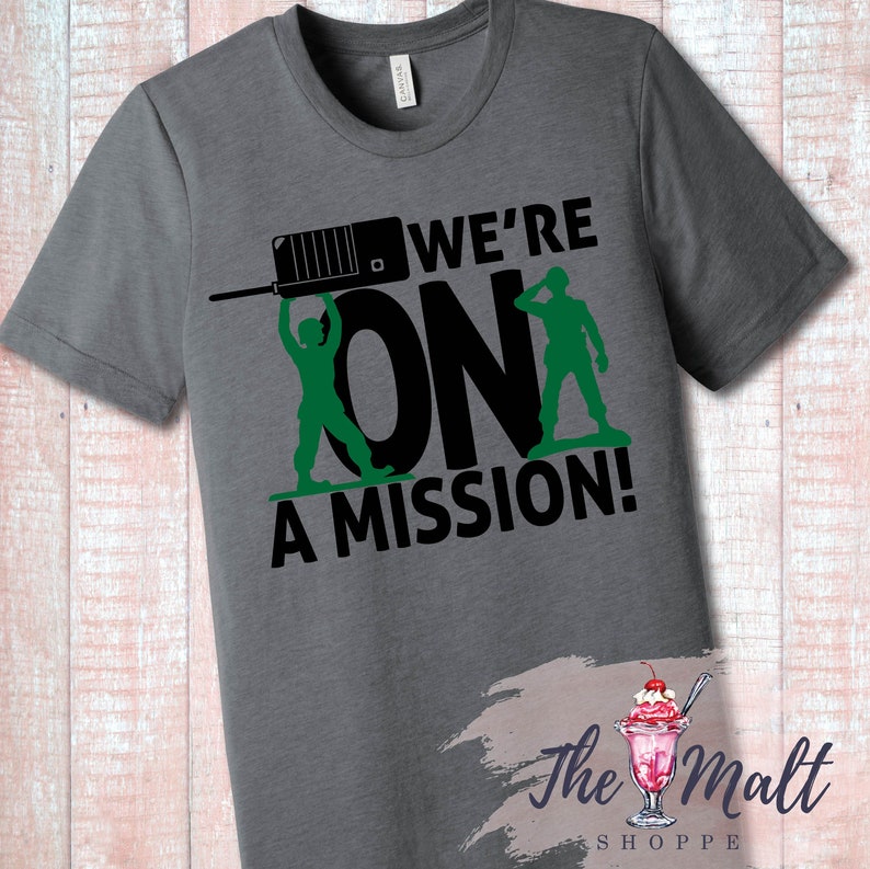 May include: A gray t-shirt with a black graphic of two toy soldiers holding a walkie-talkie and the text "We're On A Mission!"
