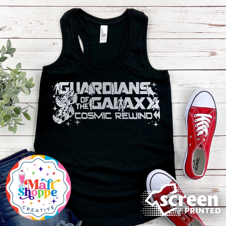 Może przedstawiać: Czarny top na ramiączkach z srebrnym nadrukiem, na kt&oacute;rym widnieje napis "Guardians of the Galaxy Cosmic Rewind". Nadruk przedstawia postacie z filmu Strażnicy Galaktyki.