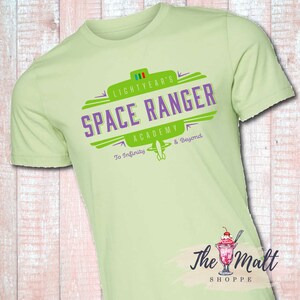 May include: A light green t-shirt with a green and purple logo that says "Lightyear's Space Ranger Academy To Infinity & Beyond".