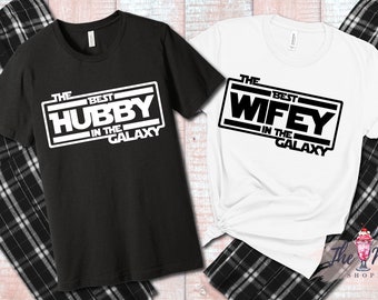 Könnte beinhalten: Ein Set aus zwei schwarzen und weißen T-Shirts mit dem Aufdruck "The Best Hubby in the Galaxy" und "The Best Wifey in the Galaxy". Die Shirts werden mit schwarzen und weißen karierten Schlafanzügen kombiniert.