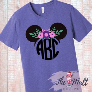 May include: Purple t-shirt featuring a black Mickey Mouse-inspired design with floral accents and the letters "ABC" in a circular monogram. The shirt is made of a soft material and is suitable for casual wear.