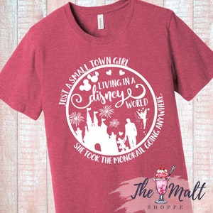 May include: Red t-shirt with a white graphic design of a castle, fireworks, and the text "Just a small town girl living in a disney world she took the monorail going anywhere."