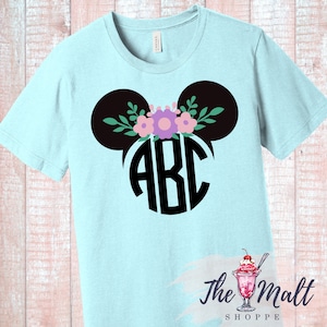 May include: Light blue t-shirt with a black Mickey Mouse ears design with a floral wreath and a black circle monogram with the letters "ABC".