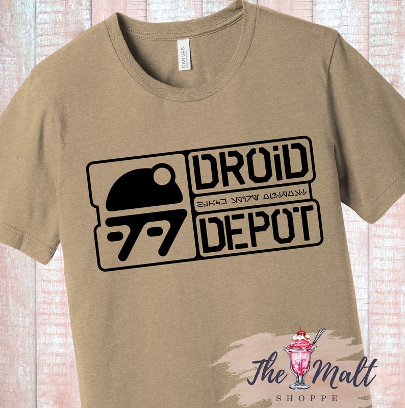 May include: A tan t-shirt with a black graphic of a droid depot logo. The logo features a stylized image of a droid head and the text "Droid Depot" in black.