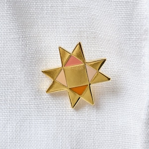 Könnte beinhalten: Eine goldene sternförmige Anstecknadel mit einem geometrischen Design in Rosa-, Orange- und Gelbtönen.