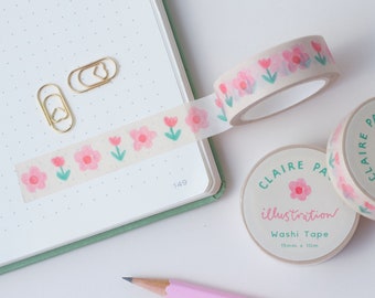 May include: Two rolls of floral washi tape with the text "Claire Paul illustration Washi Tape 15mm x 10m" on the label. The tape features a pink flower and green stem design.