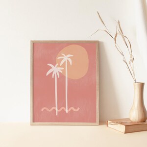May include: A framed print with a minimalist design featuring two palm trees and a sun in shades of pink, orange, and white against a peach background.