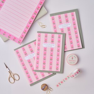 May include: Three pink and green greeting cards with the text "you are blooming wonderful" on each card. The cards are surrounded by gold paper clips, a small spool of pink and green floral washi tape, and a pair of gold scissors.