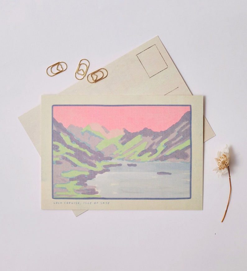 May include: A postcard with a pastel pink, green, and blue illustration of a mountain range and a lake. The text "Loch Coruisk, Isle of Skye" is printed at the bottom of the postcard.