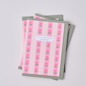 May include: A pink and green card with a pattern of pink tulips. The card has the text "you are blooming wonderful" on it.