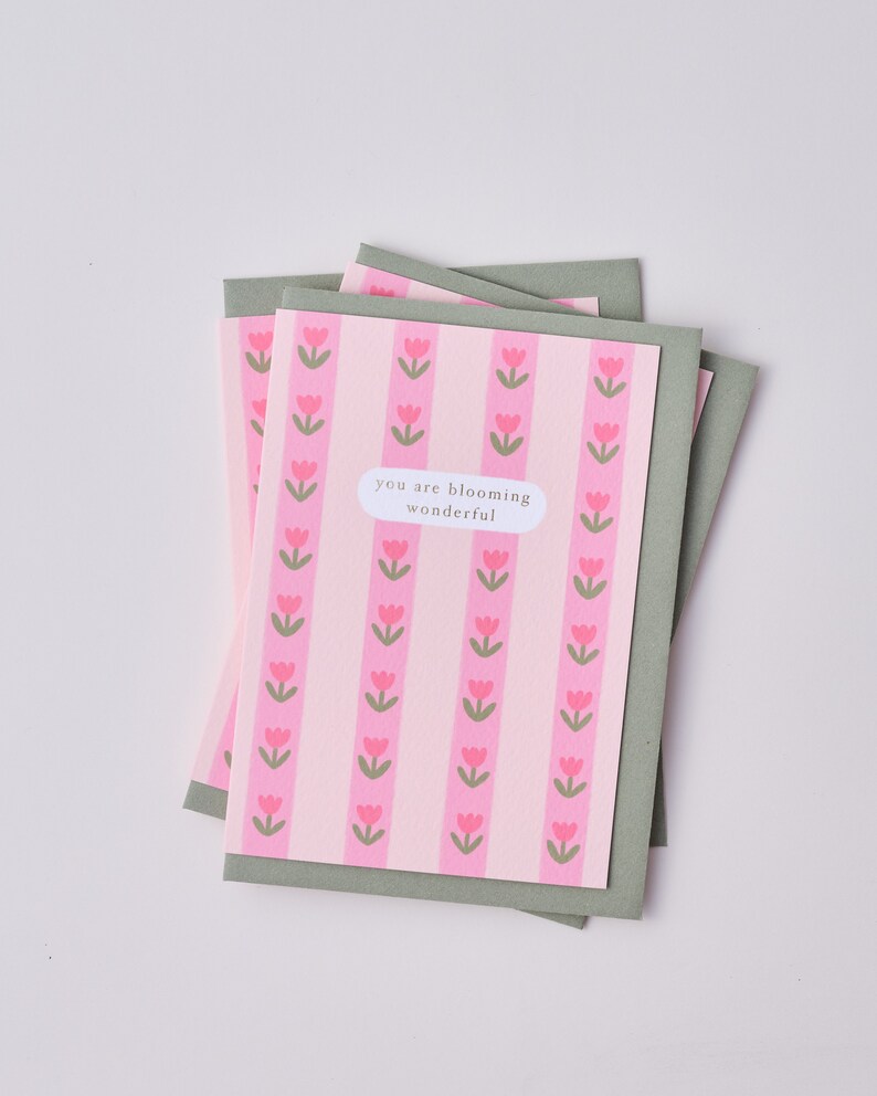 May include: A pink and green card with a pattern of pink tulips. The card has the text "you are blooming wonderful" on it.