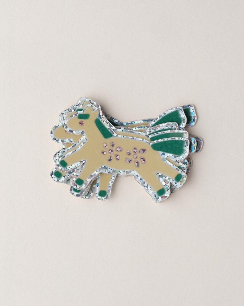 May include: A stack of glittery gold and green horse stickers. The horse has a green mane and tail and is decorated with pink flowers.