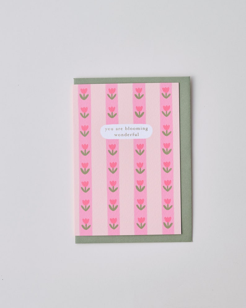 May include: A pink and green card with a repeating pattern of pink tulips. The card has the text "you are blooming wonderful" in a white circle.