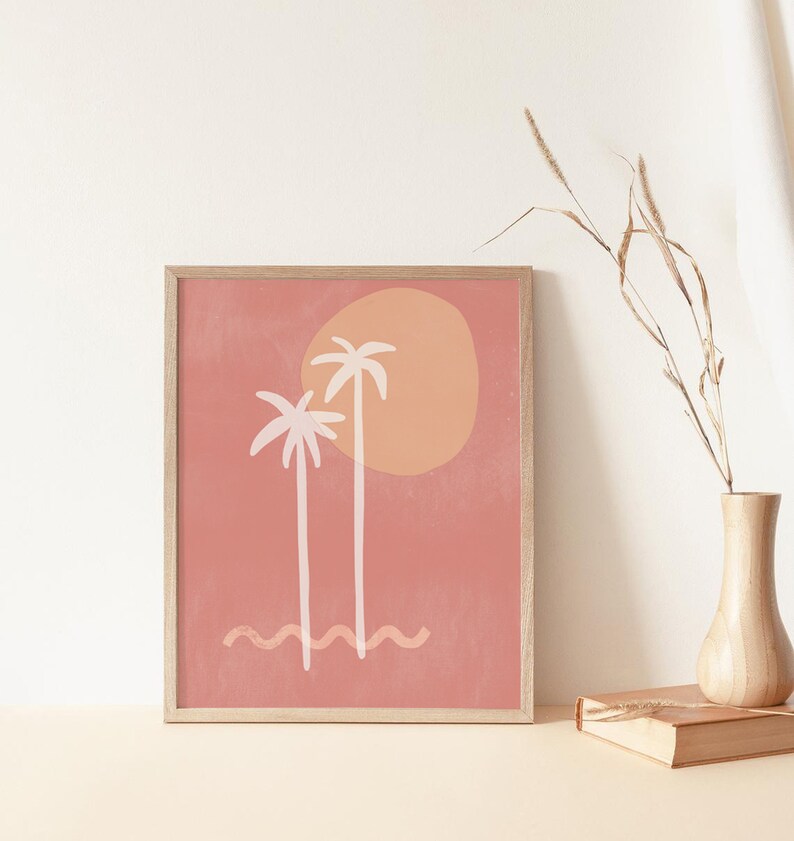 May include: A framed print with a minimalist design featuring two palm trees and a sun in shades of pink, orange, and white against a peach background.