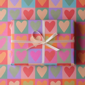 May include: A present wrapped in patterned paper with a white ribbon and bow. The paper and gift feature a repeating design of colourful hearts in squares of orange, pink, green, purple, and red.