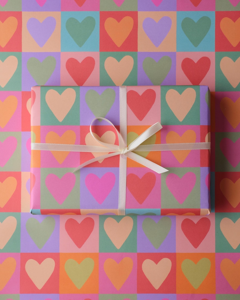 May include: A present wrapped in patterned paper with a white ribbon and bow. The paper and gift feature a repeating design of colourful hearts in squares of orange, pink, green, purple, and red.