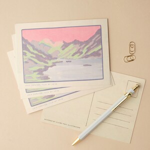 May include: A stack of postcards with a colorful illustration of a mountain range and a lake. The text on the postcard reads "Loch Crevier, Isle of Skye" and "Designed by Claire Paul Illustration".