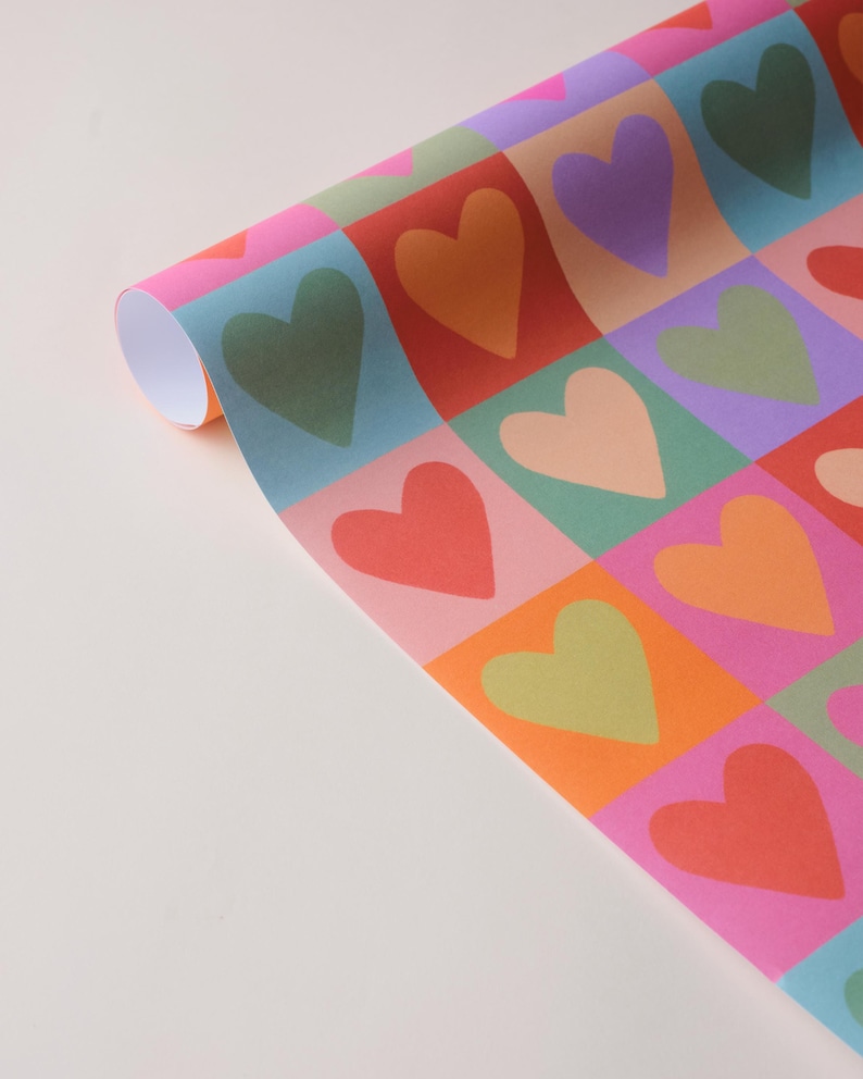 May include: Rolled sheet of wrapping paper featuring a repeating pattern of hearts in squares. The hearts are in shades of green, orange, red, pink, and purple. The background squares are in pink, blue, and orange.