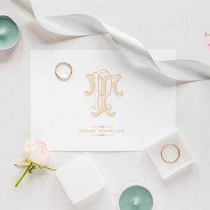 May include: A white card with a gold monogram of the letters "JT" in a decorative font. The card is surrounded by white ribbon, a small white rose, and two gold rings.