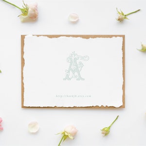 Puede incluir: Un monograma azul claro con la letra "A" en un diseño floral decorativo. El monograma está sobre un fondo blanco con un borde marrón. La imagen está rodeada de rosas y pétalos rosas.