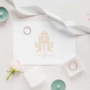 May include: A white card with a gold monogram of the letters "AA" in a decorative font. The card is surrounded by white ribbon, a white ring box, a pink rose, and teal candles.