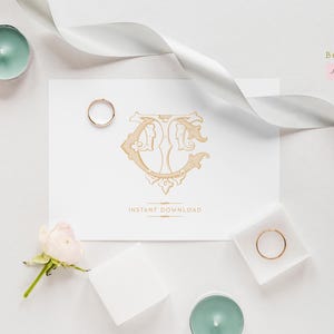 May include: A white card with a gold monogram of the letters "TC" in a decorative font. The card is surrounded by white ribbon, a white square box, a small white square with a gold ring, and a small white square with a gold ring. There are also two teal candles on the white surface.