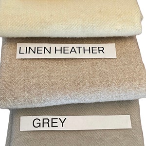May include: A stack of fabric swatches in various colors: white, primitive natural, linen heather, grey, and black. Each swatch has a label with its color name. The fabrics appear to be woven.