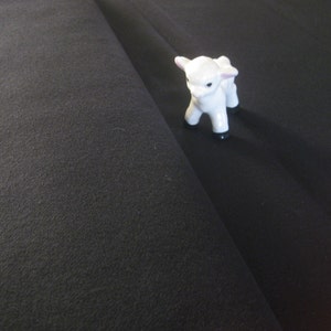 May include: A white porcelain figurine of a lamb standing on a black surface.