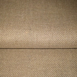 May include: Close-up of a tan-colored woven fabric with a textured surface. The fabric is folded, revealing a seam. The weave pattern is visible, creating a grid-like appearance. The material appears to be sturdy.