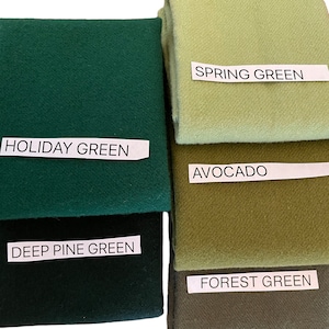 May include: A collection of folded fabric swatches in various shades of green. The swatches are labeled with names like "Holiday Green," "Spring Green," and "Avocado." The colors range from deep forest tones to lighter, pastel hues.