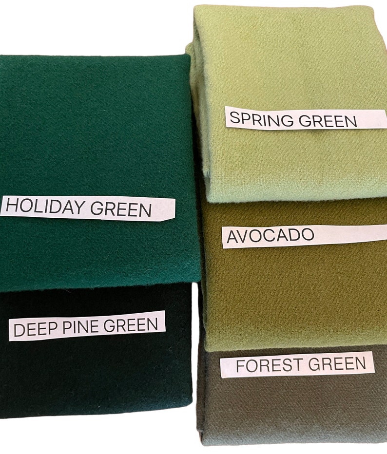 May include: A collection of folded fabric swatches in various shades of green. The swatches are labeled with names like "Holiday Green," "Spring Green," and "Avocado." The colors range from deep forest tones to lighter, pastel hues.