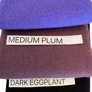 May include: A stack of fabric swatches in shades of purple. The top swatch is violet, followed by medium plum, and dark eggplant. Each swatch has a label with the color name in white text.