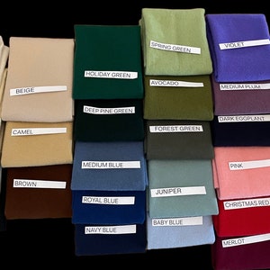 May include: A collection of folded fabric swatches in various colors, including white, beige, green, blue, and red. Each swatch has a label with its color name, such as "White," "Holiday Green," and "Merlot." The swatches are arranged on a black background.