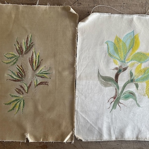 May include: Two fabric squares with embroidered floral designs. One shows a branch with green, yellow, and brown leaves on a beige background. The other depicts a flower with yellow and blue petals on a white background.