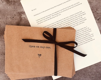 May include: A stack of brown envelopes tied with a black ribbon. The top envelope has the text "Open on day one." written on it with a heart drawn below the text.