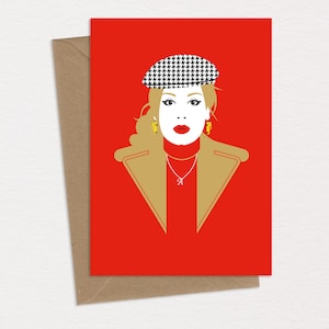 Puede incluir: Una tarjeta roja con una mujer que lleva un sombrero de patrón blanco y negro, una chaqueta dorada y un collar dorado con un colgante de la letra A. La mujer tiene el pelo rubio y los labios rojos.