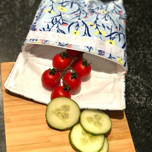May include: A blue and white floral reusable food storage bag with a white lining. The bag is open and filled with red tomatoes and sliced cucumbers on a wooden chopping board.