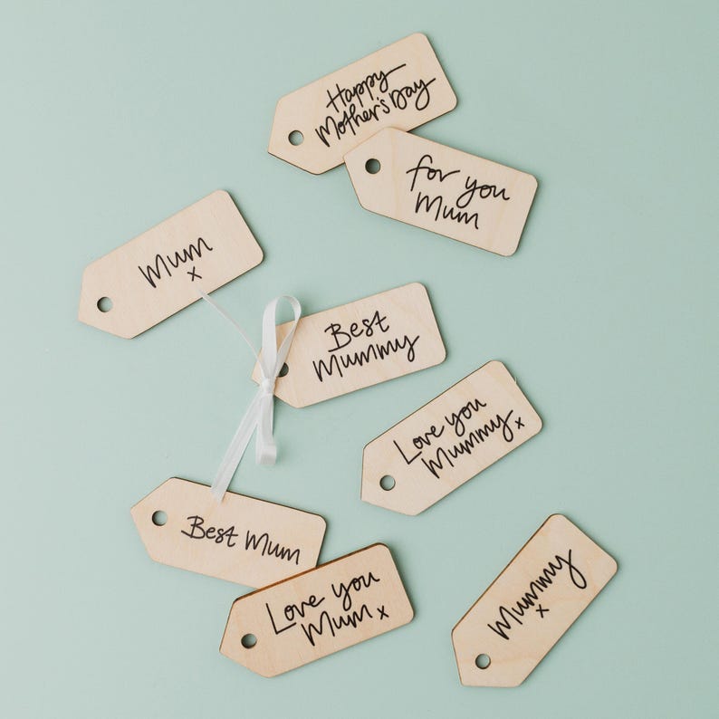 May include: Eight wooden gift tags with handwritten messages for Mother's Day. The tags are light brown and have black ink. The messages include "Mum", "Best Mummy", "Love you Mummy", "Happy Mother's Day", "For you Mum", and "Best Mum".