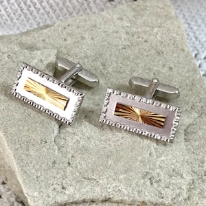 May include: A pair of silver cufflinks with a gold rectangular design in the center. The cufflinks have a textured border.