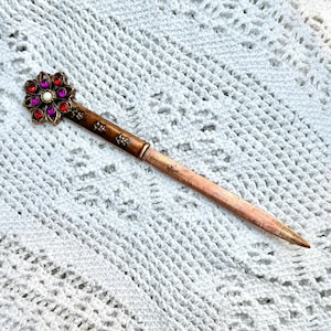 Abrecartas de cobre. Mango con estampado floral en relieve. Parte superior en forma de flor con diamantes de imitación morados y rojos. 16 cm