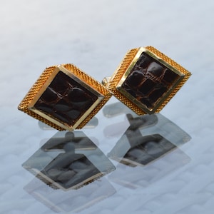 May include: A pair of gold cufflinks with a brown crocodile pattern. The cufflinks are in the shape of a diamond.