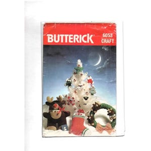 May include: A Butterick 6053 craft pattern envelope featuring a night scene with a crescent moon. The image displays a white Christmas tree with small ornaments, a brown reindeer figure, a red stocking, and a green wreath with small bears.