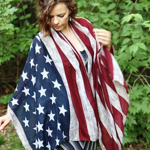 May include: A woman wearing a striped dress and a scarf patterned with the American flag. The scarf is draped over her shoulders and is flowing in the wind.
