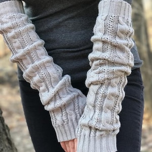 May include: A pair of gray knitted arm warmers with a cable knit pattern. The arm warmers are long and reach to the elbows.