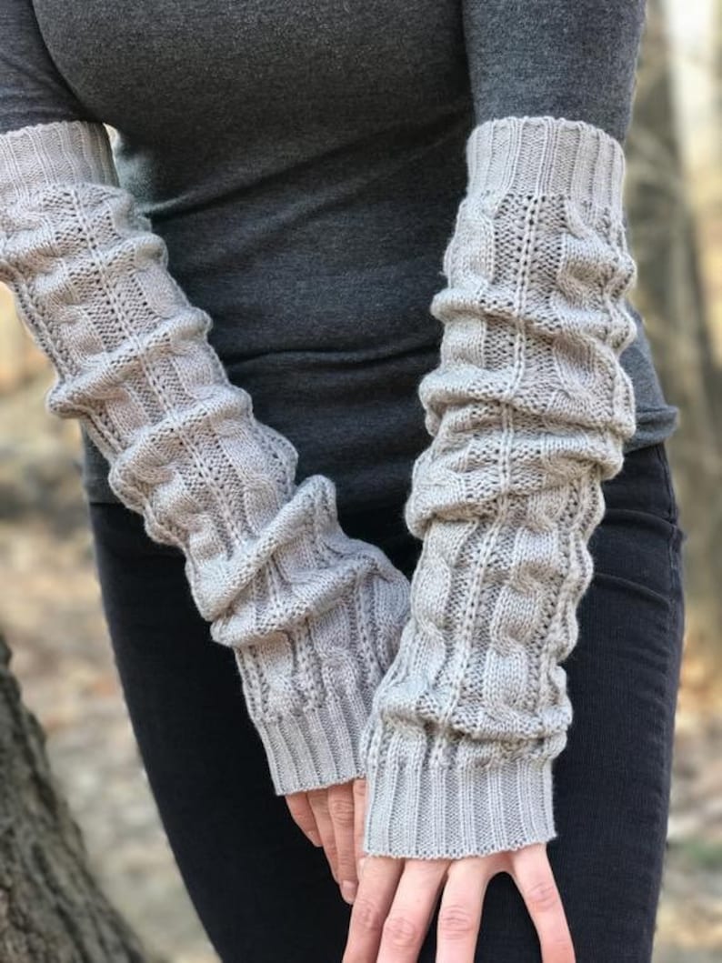 May include: A pair of gray knitted arm warmers with a cable knit pattern. The arm warmers are long and reach to the elbows.