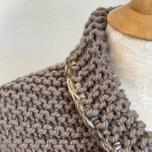 Pu&ograve; includere: Un cardigan di maglia marrone con un bordo bianco e marrone intorno al collo.