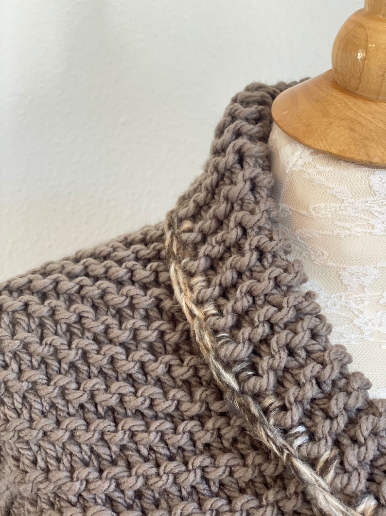 Pu&ograve; includere: Un cardigan di maglia marrone con un bordo bianco e marrone intorno al collo.